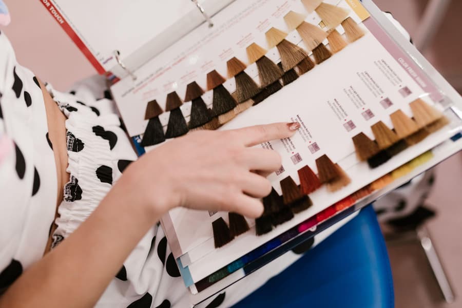A client's finger on a hair colour swatch chart of blonde and brown tones