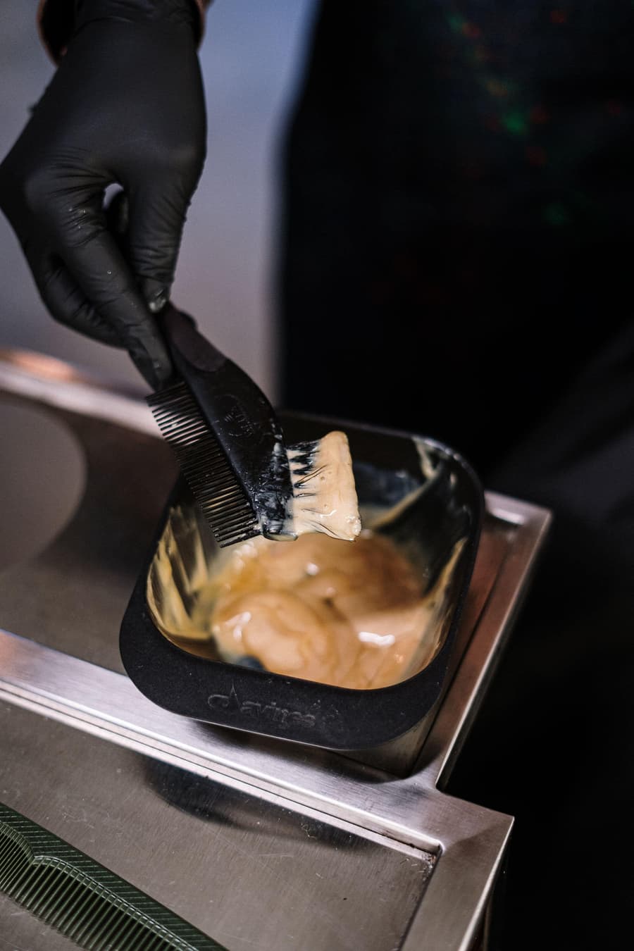 Gloved hands mixing a honey-toned colour in a black bowl