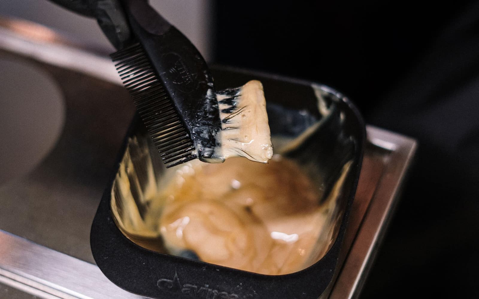 Gloved hands mixing a honey-toned colour in a black bowl